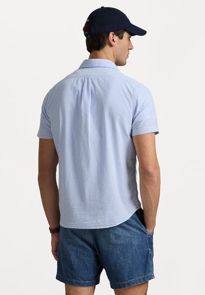 Chemise à manches courtes, col montant, de couleur bleu clair avec des rayures blanches. Tissu tissé, coupe décontractée avec un ourlet arrondi. Associée à un short en jean.
