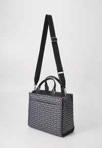 Saco tote DKNY preto e cinza com padrão de logotipo repetido, alças curtas e alça de ombro longa ajustável em fundo simples.