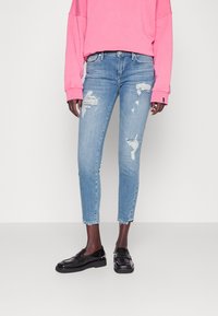 Jasnoniebieskie, postarzane dżinsy z przetarciami, slim fit, skrócone nad kostką, w połączeniu z różowym, oversize'owym swetrem i czarnymi loafersami.