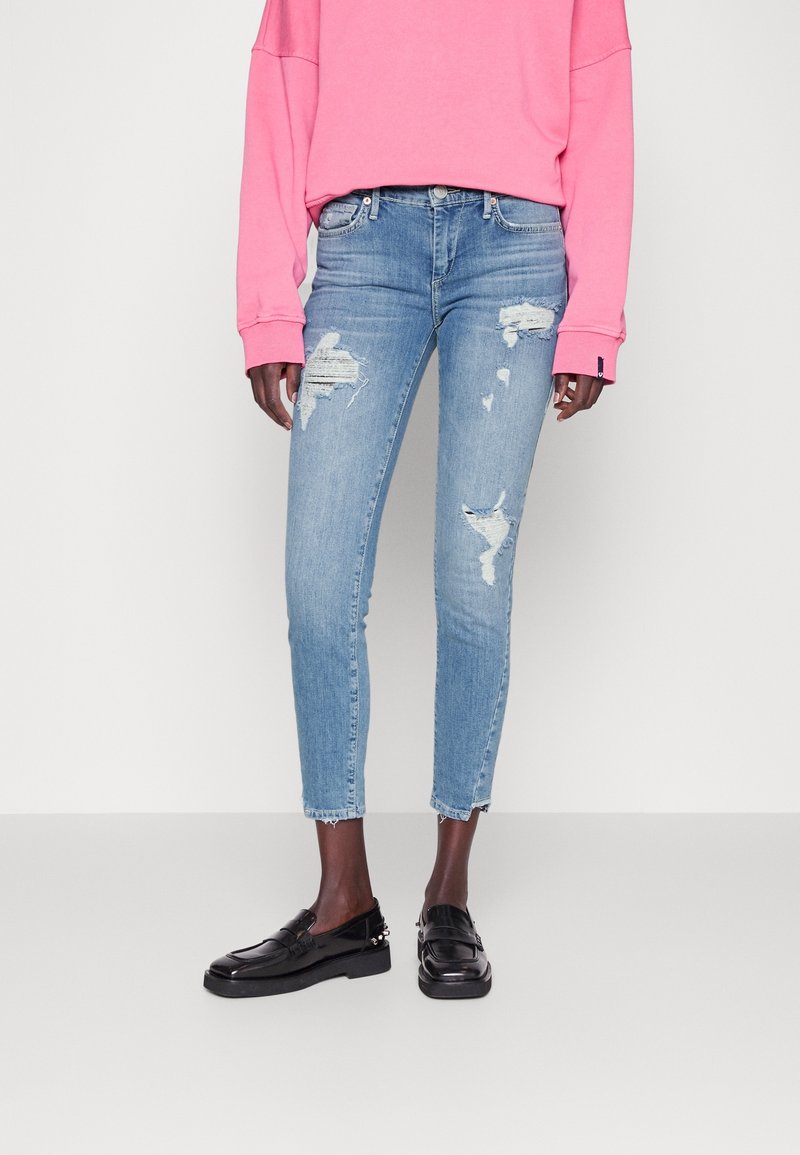 Jasnoniebieskie, postarzane dżinsy z przetarciami, slim fit, skrócone nad kostką, w połączeniu z różowym, oversize'owym swetrem i czarnymi loafersami.