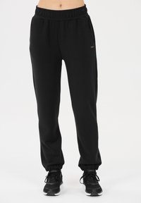 Zwarte trainingsbroek met een elastische tailleband, tapse enkelboorden en zijzakken. Gemaakt van zachte stof met een subtiele textuur. Minimalistisch ontwerp.