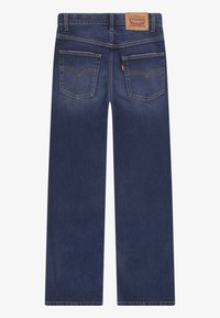 Dark blue denim jeans with straight leg cut, reinforced stitching, visible back pockets, and a classic logo patch on the waistband.