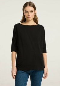 Czarna, luźna bluzka z dekoltem łódki, rękawami do trzech czwartych i miękką fakturą; połączona z niebieskimi dżinsami.