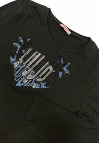 T-shirt nera a maniche lunghe con un design di borchie che presenta stelle blu e nere, e un elemento grafico in argento e blu sulla parte anteriore.
