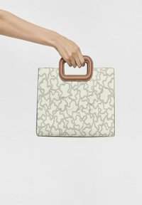 Bolso tote blanco con un diseño abstracto gris claro, que presenta un asa rectangular marrón, fabricado con un material texturizado.