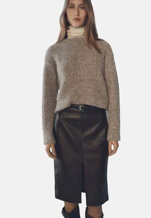 Grauer Wollpullover mit lockerem Schnitt und Rundhalsausschnitt, kombiniert mit einem schwarzen Leder-Midirock mit Schlitz vorne.