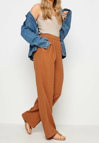 Jasnobrązowe spodnie o szerokich nogawkach z fakturowanym wykończeniem, zestawione z beżowym topem na ramiączkach z prążkowanej tkaniny i oversize'ową niebieską kurtką dżinsową.