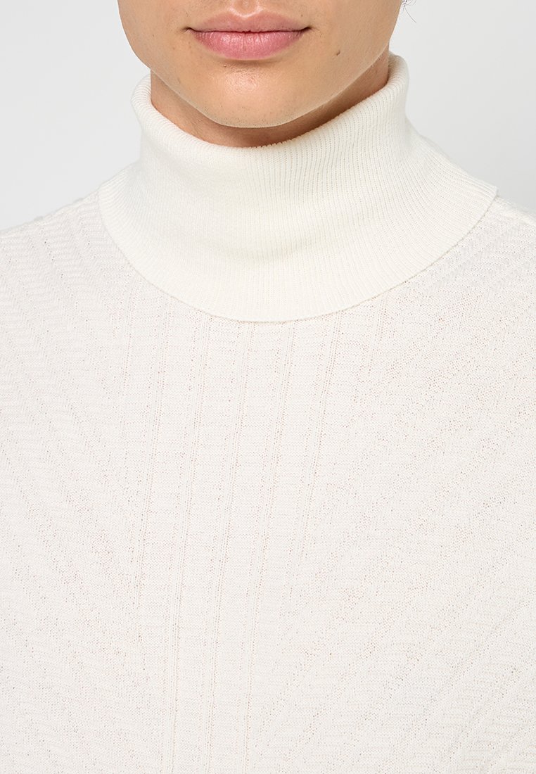 Maglione bianco a collo alto a coste, caratterizzato da una texture morbida e una leggera lucentezza. Il design include righe verticali per un tocco di dettaglio in più.