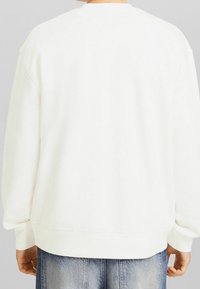 Vit sweatshirt med rundad halsringning och ribbade ärmslut. Har en avslappnad passform och mjuk textur. Baksidan visar inga tryck eller mönster.