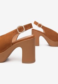 Chaussures slingback en daim brun avec un robuste talon block beige. Présentent une boucle ronde en argent et une finition lisse sur le talon.