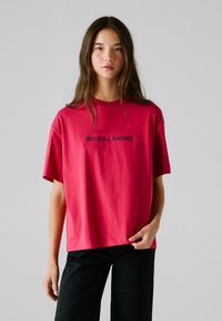 Röd T-shirt med korta ärmar, med texten "RED BULL RACING" i svart, gjord av bomull, matchad med svarta byxor.