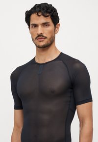 Schwarzes kurzärmliges Netzshirt mit taillierter Passform und Rundhals. Verfügt über ein kleines Etikett am Kragen und einen strukturierten, atmungsaktiven Stoff.