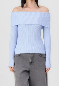 Maglione a coste azzurro chiaro con scollo a barra e maniche lunghe, realizzato in un tessuto morbido, abbinato a pantaloni grigi a gamba larga.
