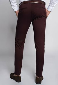 Burgundowe slim-fit spodnie o gładkiej fakturze, z paskiem, tylnymi kieszeniami i stylizowane na brązowe zamszowe buty.