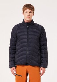 Sort puffer-jakke med quiltet design, lynlåslukning foran, opretstående krave og sidelommer, kombineret med orange bukser.
