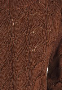 Brązowy sweter dzianinowy z wyraźnym wzorem i ażurowymi detalami. Materiał jest miękki, z żebrowanym dekoltem i starannym szyciem.