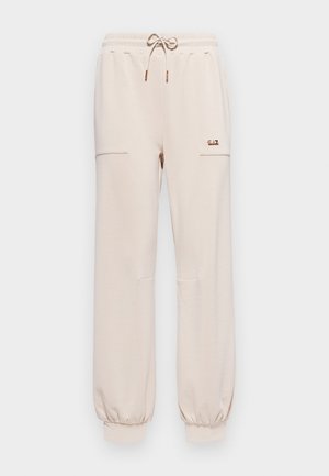 Pantaloni da sudore di un beige chiaro con vita elastica, cordino e caviglie con polsini. Presentano due tasche laterali e un piccolo dettaglio del logo.