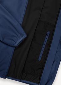 Veste bleue avec poignet élastique et doublure intérieure noire avec une poche verticale zippée sur un côté.