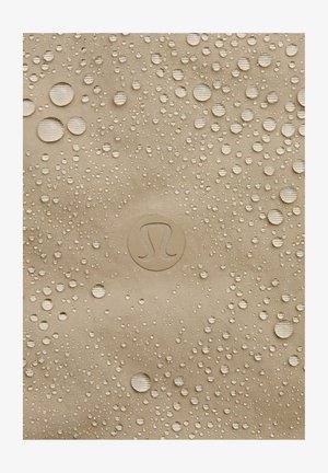 Beige, teksturoitu kangas, jossa on lukuisia vesipisaroita; keskellä on pyöreä logo. Materiaali vaikuttaa vedenkestävältä.