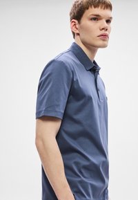 Tmavomodrá polokošeľa s krátkym rukávom, klasickým límcom, dvoma gombíkmi a hladkou textúrou látky, s jemným logom na hrudi.