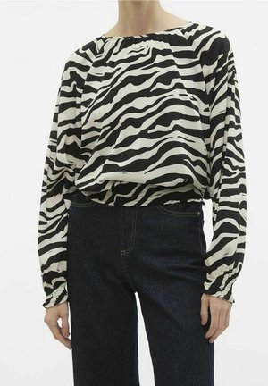 Blouse à motifs zèbre noir et blanc avec une coupe ample, un ourlet élastiqué et des manches ballon, associée à un jean en denim foncé.