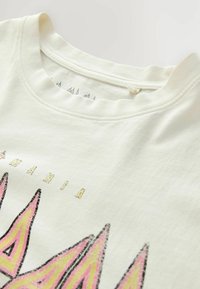 Off-white T-shirt med krave med synlige sømme og en del af et pink og gult solburst-grafik samt delvist "MIA" tekst ovenfor.