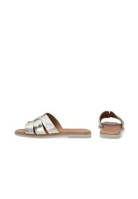 Metallisch silberne Riemensandalen mit drei breiten Riemen, einer flachen Sohle und einer braunen gepolsterten Innensohle. Strukturierte Oberfläche der Riemen; offenes Rückendesign.