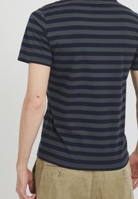 Tílko v námořnické a šedé pruhované barvě s krátkým rukávem, vyrobené z bavlny, s kulatým výstřihem, zakulaceným spodním lemem a logem na bočním švu.