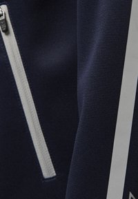 Tessuto blu navy con una finitura testurizzata, caratterizzato da una zip argentata e dettagli con striscia verticale argentata lungo il lato.