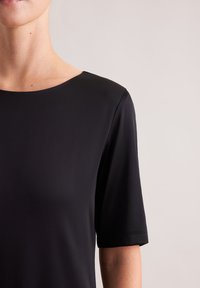 Czarna bluzka z krótkim rękawem o łódkowym dekolcie, gładkiej fakturze i swobodnym kroju. Bez widocznych logo ani wzorów.