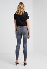 Vaqueros ajustados de color gris oscuro con una cintura media, bolsillos traseros y una etiqueta de cinturón de cuero marrón. Combinados con una camisa negra y tacones con tiras.