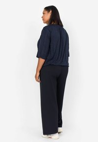 Top a righe navy con maniche corte abbinato a pantaloni larghi neri. Il top presenta un design geometrico e una vestibilità comoda.