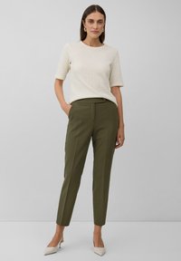 Top corto a maniche corte in crema chiaro con texture, abbinato a pantaloni sartoriali verdi oliva. Modello con scarpe beige a punta. Design semplice e moderno.