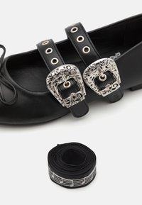 Black leather shoes featuring two decorative silver buckles and matching straps. Accompanied by a roll of black elastic with music notes pattern.