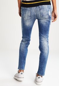 Pantalones vaqueros de denim azul claro con un ajuste slim, textura desgastada y bolsillos traseros. Combinados con zapatillas Nike Air blancas.