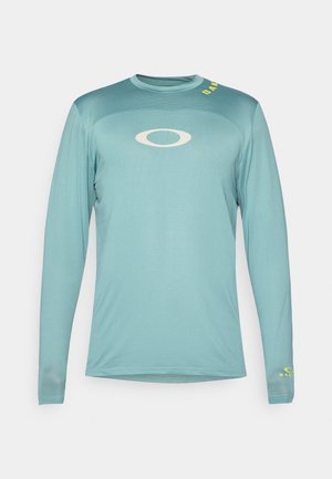 Heledad spordipaita helesinises kangas, millel on tekstuuriline muster. Rinnal on valge logo ja varrukal kollane kiri.