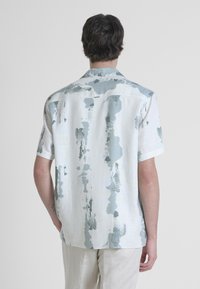 Camicia a maniche corte in tessuto leggero, con uno sfondo bianco e sottili motivi di spruzzature grigio-blu. Collo classico e vestibilità rilassata.