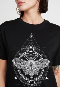 Sort bomulds t-shirt med et hvidt grafisk print af en møl omgivet af geometriske former og himmellegemer. Korte ærmer og rund hals.
