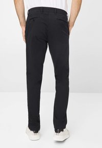 Schwarze Baumwollhosen mit schmaler Passform, ausgestattet mit zwei Gesäßtaschen und einem sicheren Bund. Getragen mit weißen Sneakers.