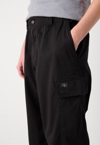 Pantalons cargo noirs en tissu mélangé coton, avec poches latérales, un patch logo et une taille élastique pour le confort.