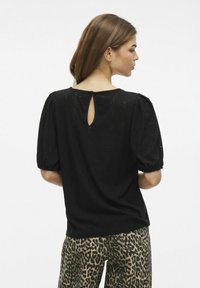 Svart topp med strukturerad tyg, puffärmar och detalj med nyckelhål i ryggen. Matchad med byxor i leopardmönster.