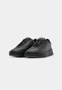 Zapatillas negras de cuero con textura suave, cuello acolchado y puntera redonda. Presentan una suela de goma gruesa y diseño de cordones.