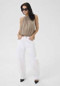 Hnědý halter top v kombinaci s volnými bílými džíny a černými lodičkami s ostrou špičkou. Top má nařasený výstřih a džíny mají přední kapsy.