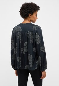 Pika varrukaga tumesinine pluus paisleimustriga, lahtise lõikega, ümara kaelusega ja kummiga mansettidega. Sile tekstuur ja voolav disain.