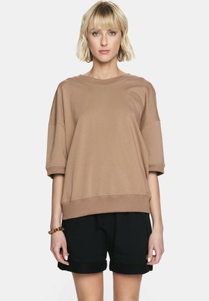 Brązowy, oversize sweter z szerokimi rękawami i okrągłym dekoltem, w połączeniu z czarnymi szortami. Miękka, przypominająca bawełnę tekstura, minimalny design.