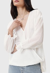 Hvid bluse i et tekstureret, let stof. Har en V-udskæring, pufærmer med elastiske manchetter og en afslappet pasform. Bæres med denim.