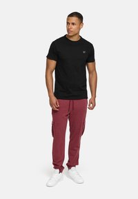 SchwarzesT-Shirt mit kurzen Ärmeln und kleinem Logo, kombiniert mit burgunderfarbenen Cargohosen mit Seitentaschen und marineblauem Kordelzug, vollendet mit weißen Sneakers.