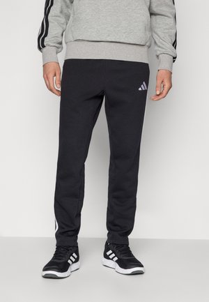 Sorte træningsbukser lavet af en bomuldsblanding, med sidelister, en tapered design og et lille hvidt Adidas-logo på låret.