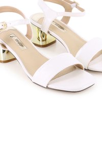 Sandalias blancas de tiras con punta cuadrada, parte superior de imitación de cuero suave y tacones de bloque acentuados en dorado. Diseño minimalista con una correa ajustable en el tobillo.