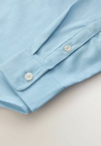 Hellblauer Hemdärmelsaum aus Stoff mit einem einzelnen weißen Knopf, verfügt über eine glatte Textur und einen schräg geschnittenen Rand am Ärmelabschluss.